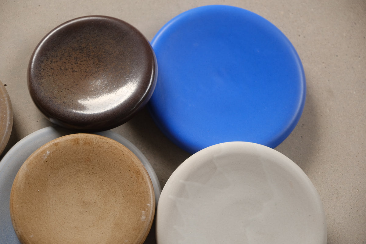 Bubble Plates arranged in a top-down cluster of four, showing smooth cobalt blue, speckled brown, tan, and pale glazes.