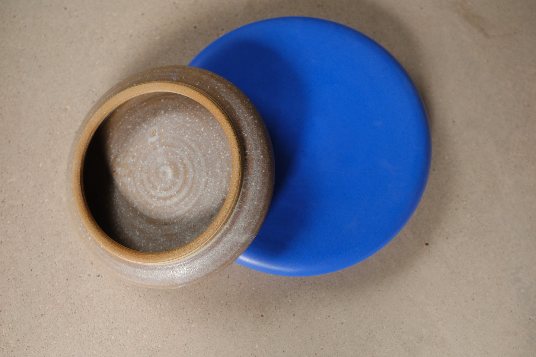 Bubble Plate in solid blue set beneath an inverted plate, exposing a raw unglazed clay foot ring and spiral base marks.