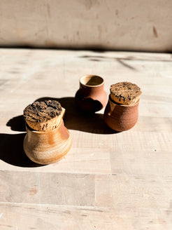 Seed jar trio from a high angle, showing one open rim between two stoppered ceramic pots on a wooden worktop.