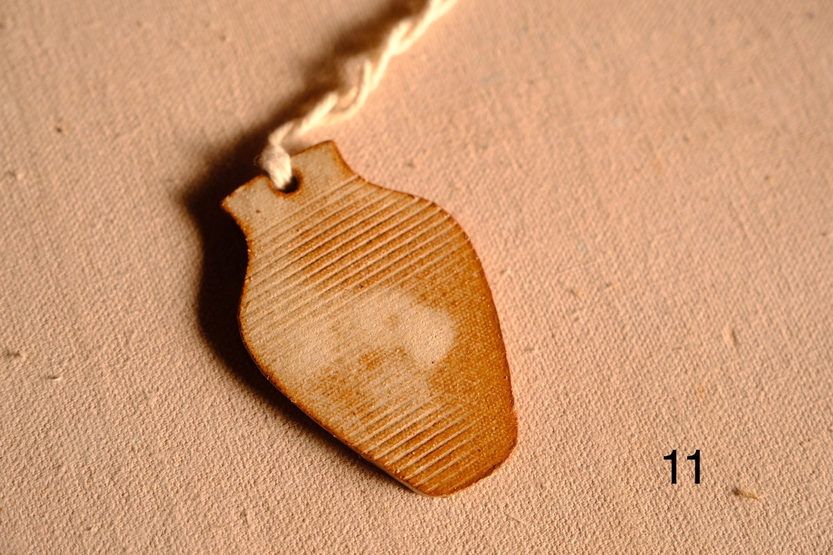 Ceramic ornament vase shape with horizontal grooved lines and subtle clay tone variations, numbered eleven on fabric.