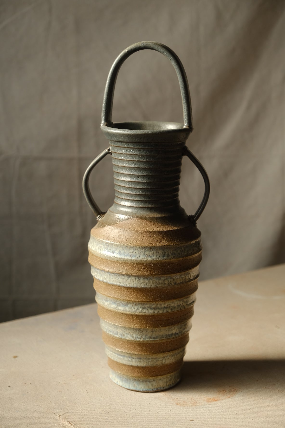 Eros Amphora ceramic vase with arched overhead handle and two side handles, lit from the right on a neutral surface.