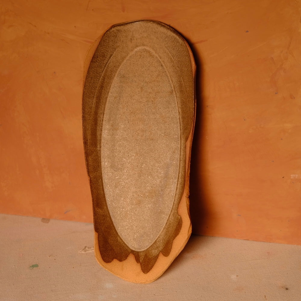 Narrow Tera Platter propped upright showing oval center glaze with dripped border and raw terracotta base.