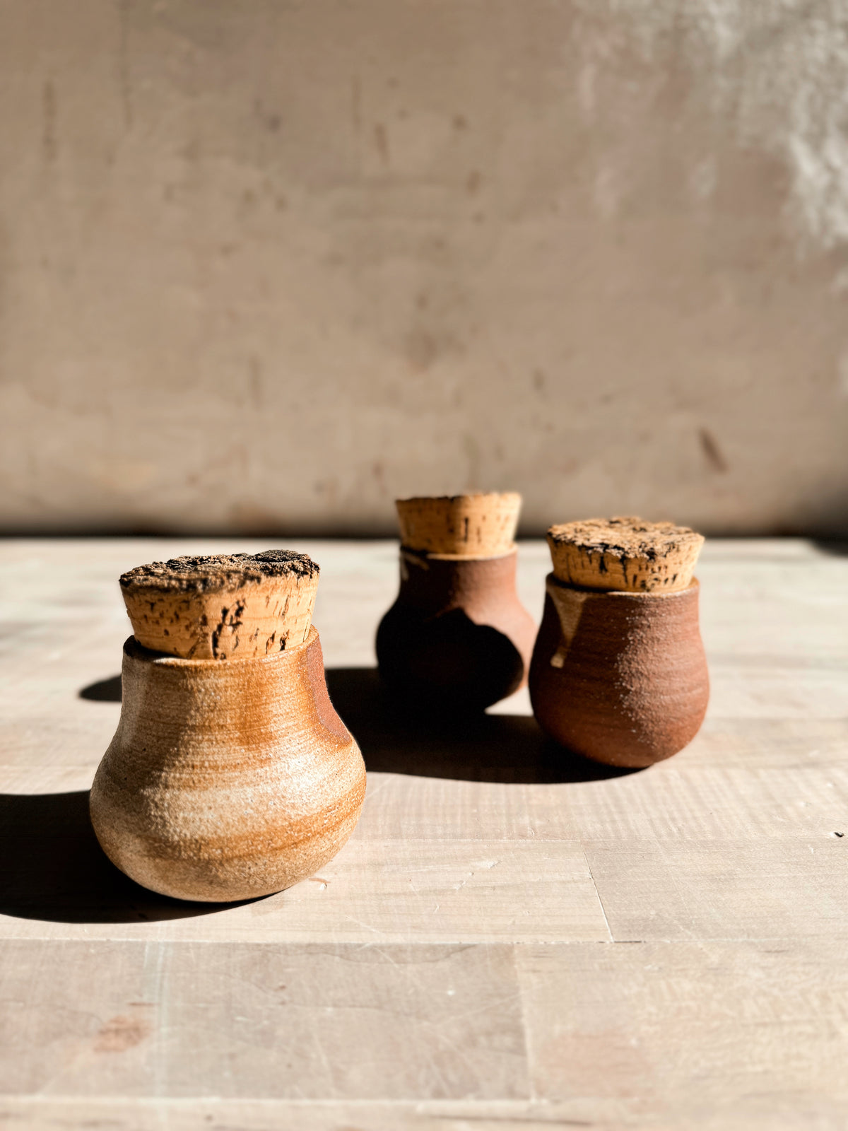 Seed jar trio with thick cork stoppers, focusing on the light textured pot in front on a wooden surface.
