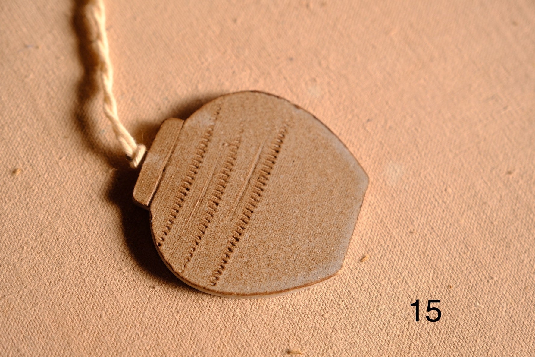 Ceramic ornament rounded vessel cutout with three vertical rows of impressed dashed stitch markings, numbered fifteen.
