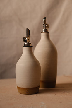 Wander Oil Bottle pair in matte off-white, small bottle centered in foreground with raw clay base stamp.