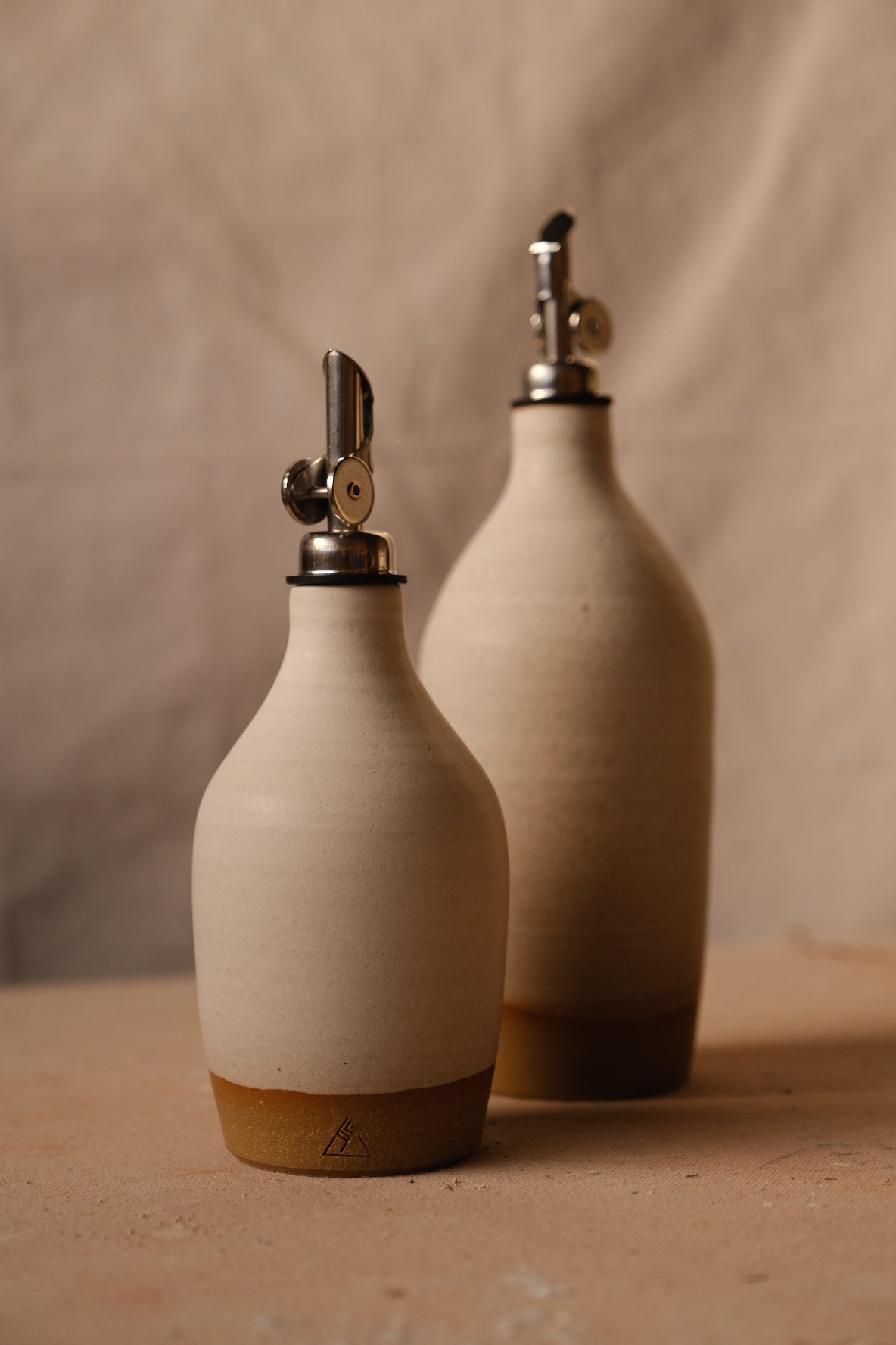 Wander Oil Bottle pair in matte off-white, small bottle centered in foreground with raw clay base stamp.