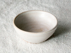 Wander Pinch Bowl in off-white glaze with subtle wheel ridges, angled view on light woven linen.
