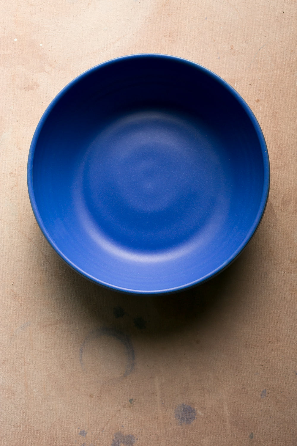 Wander Serving Bowl: top view of a bold cobalt blue stoneware bowl centered on a warm tabletop.