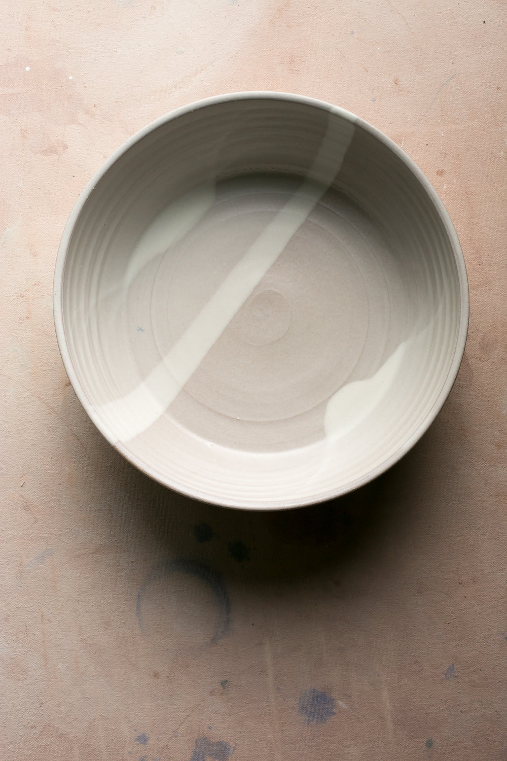 Wander Serving Bowl: top-down view of an off-white stoneware bowl featuring broad pale brushstrokes across the interior.