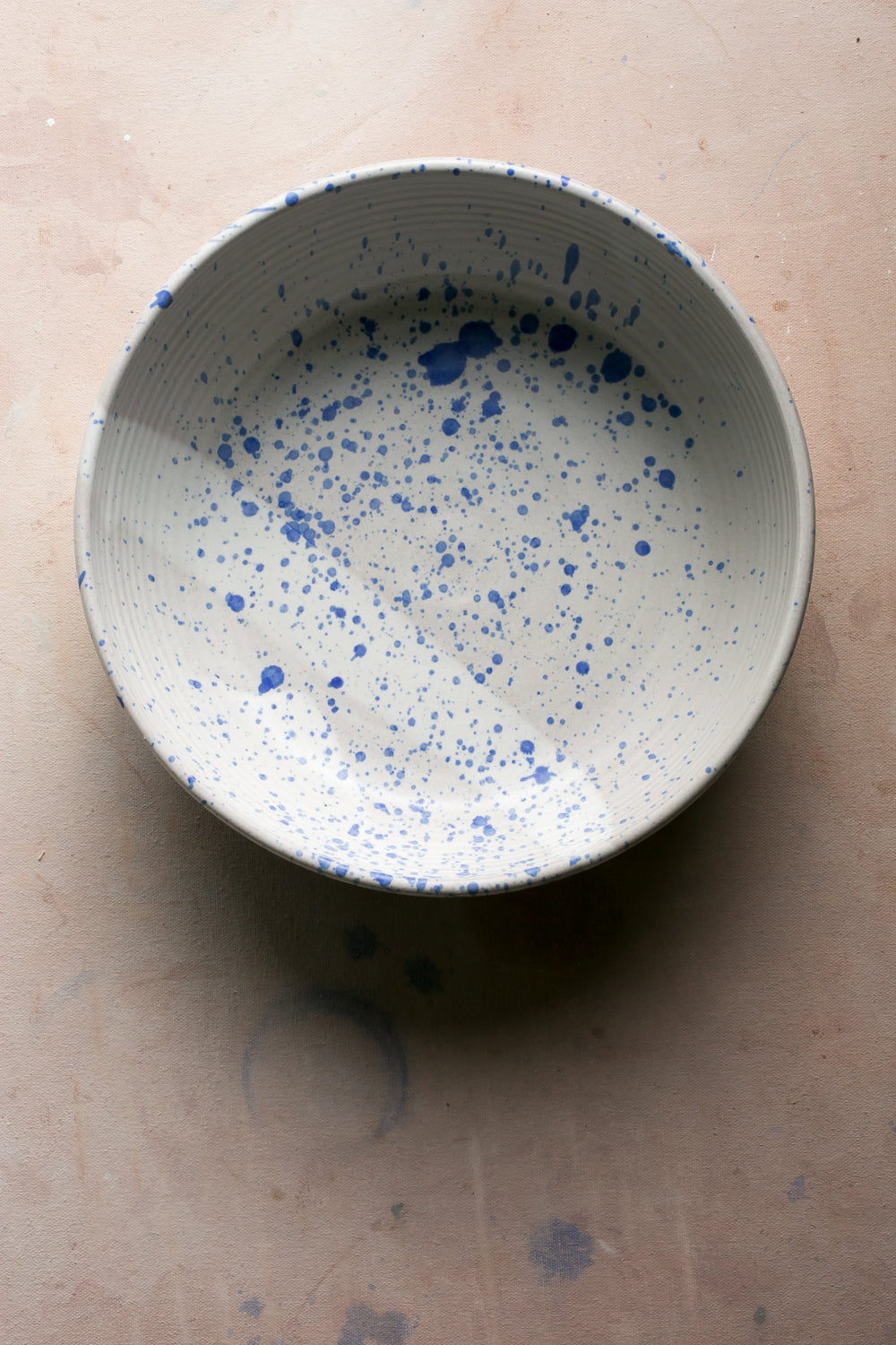 Wander Serving Bowl: overhead view of a light stoneware bowl decorated with dense blue speckles throughout.