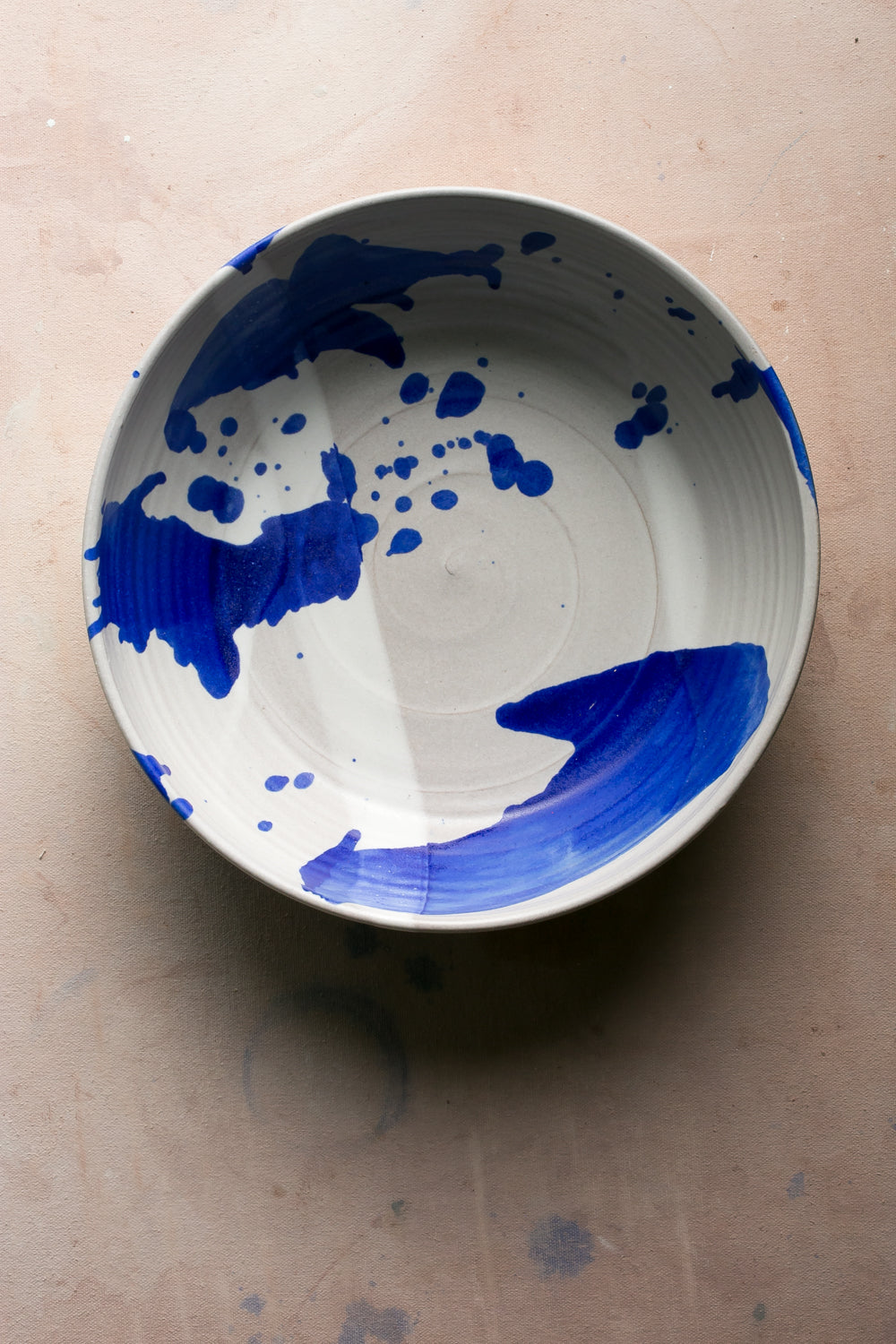 Wander Serving Bowl: overhead shot of an off-white stoneware bowl with bold abstract cobalt brushstrokes and splatter.
