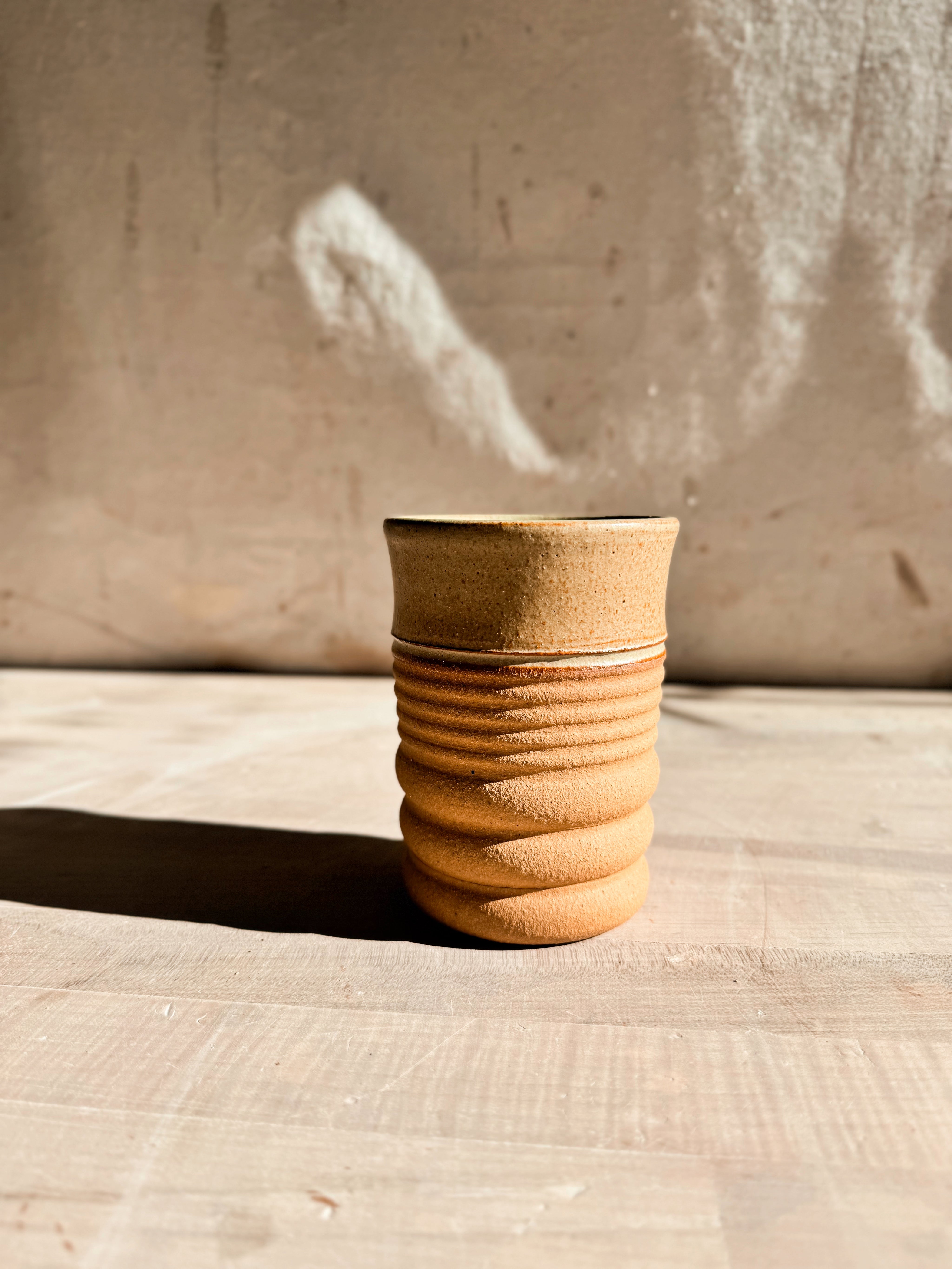 Textured Tumbler: flared-rim cup with a smooth glazed upper half and grooved raw clay base on a light wood table.