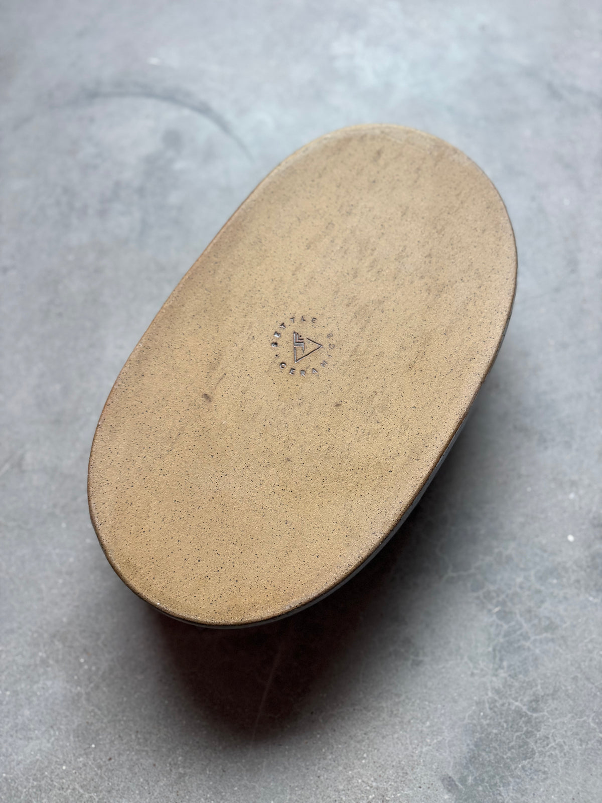 Speckle Cenote Hot Dish, overturned revealing the flat raw stoneware base stamped with the studio maker mark.