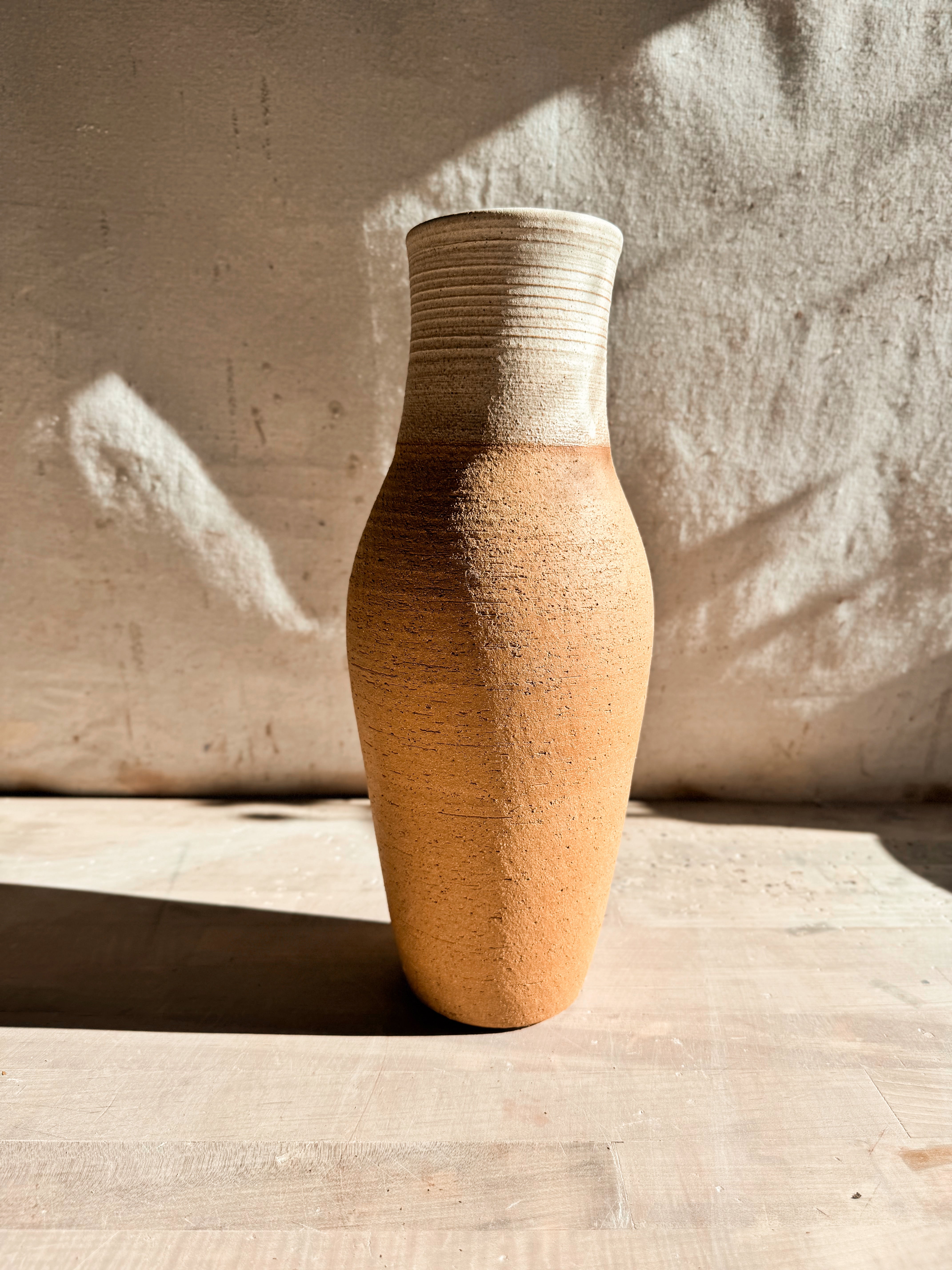 High Desert Vase in tall slender form with ridged glazed neck and raw clay body, empty on a wooden surface