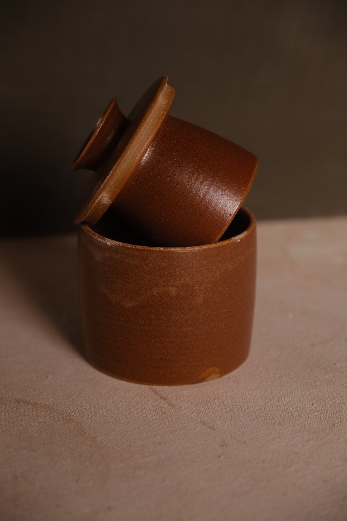 Butterbell in warm amber-brown glaze, bell lid tipped and resting inside the crock's opening, on neutral cloth.