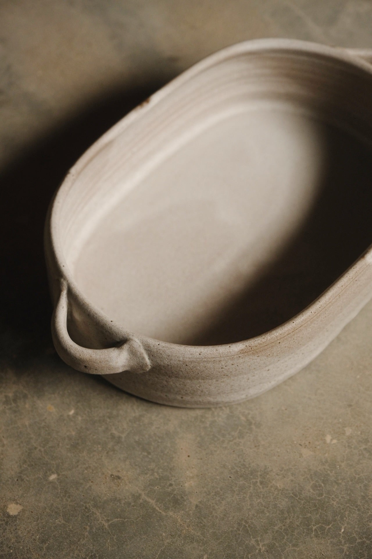 Blanca Hot Dish, high-angle view of an oval ceramic casserole with curved side handles on a mottled concrete surface.