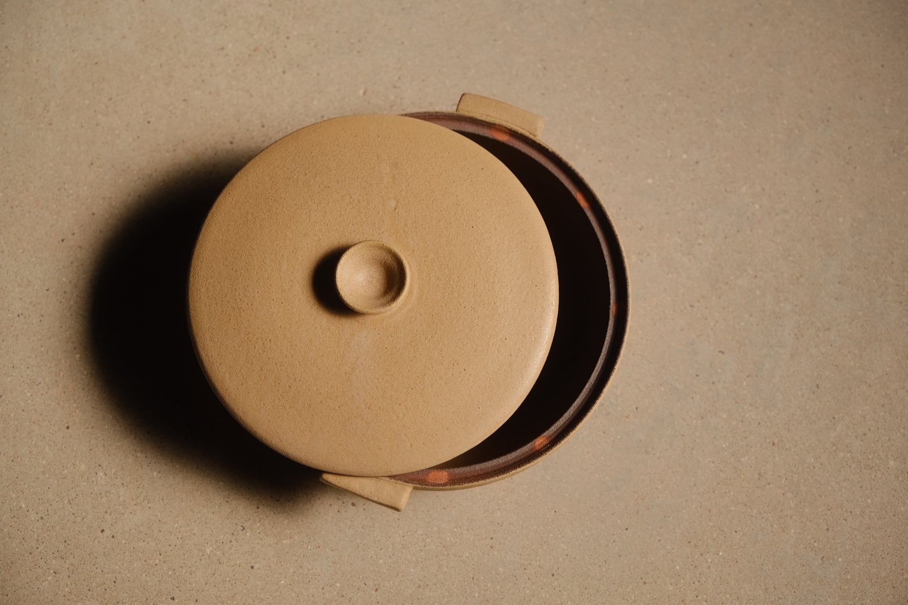 Satin Sand Lidded Hot Dish viewed from above with round lid set askew, revealing the dark interior glaze.