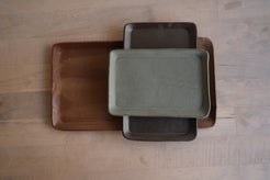 Trinket Tray stack of three rectangular stoneware trays arranged perpendicular on a light wood surface, overhead view.