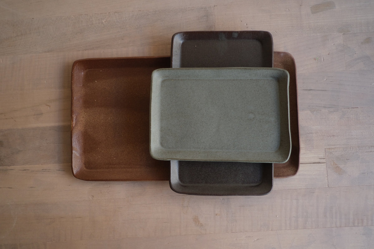 Trinket Tray stack of three rectangular stoneware trays arranged perpendicular on a light wood surface, overhead view.
