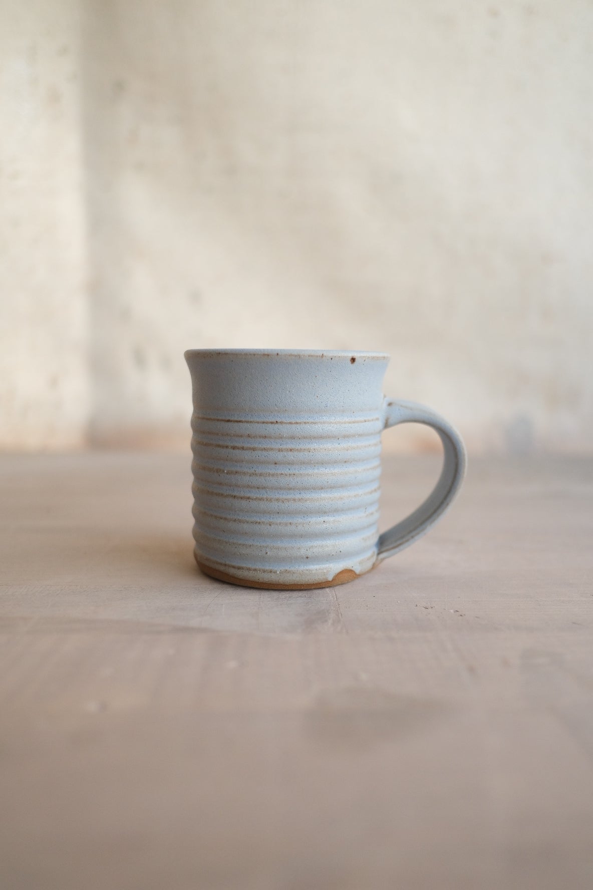 The Little Mug: side profile of a ribbed ceramic espresso cup with handle and raw clay foot on a table.