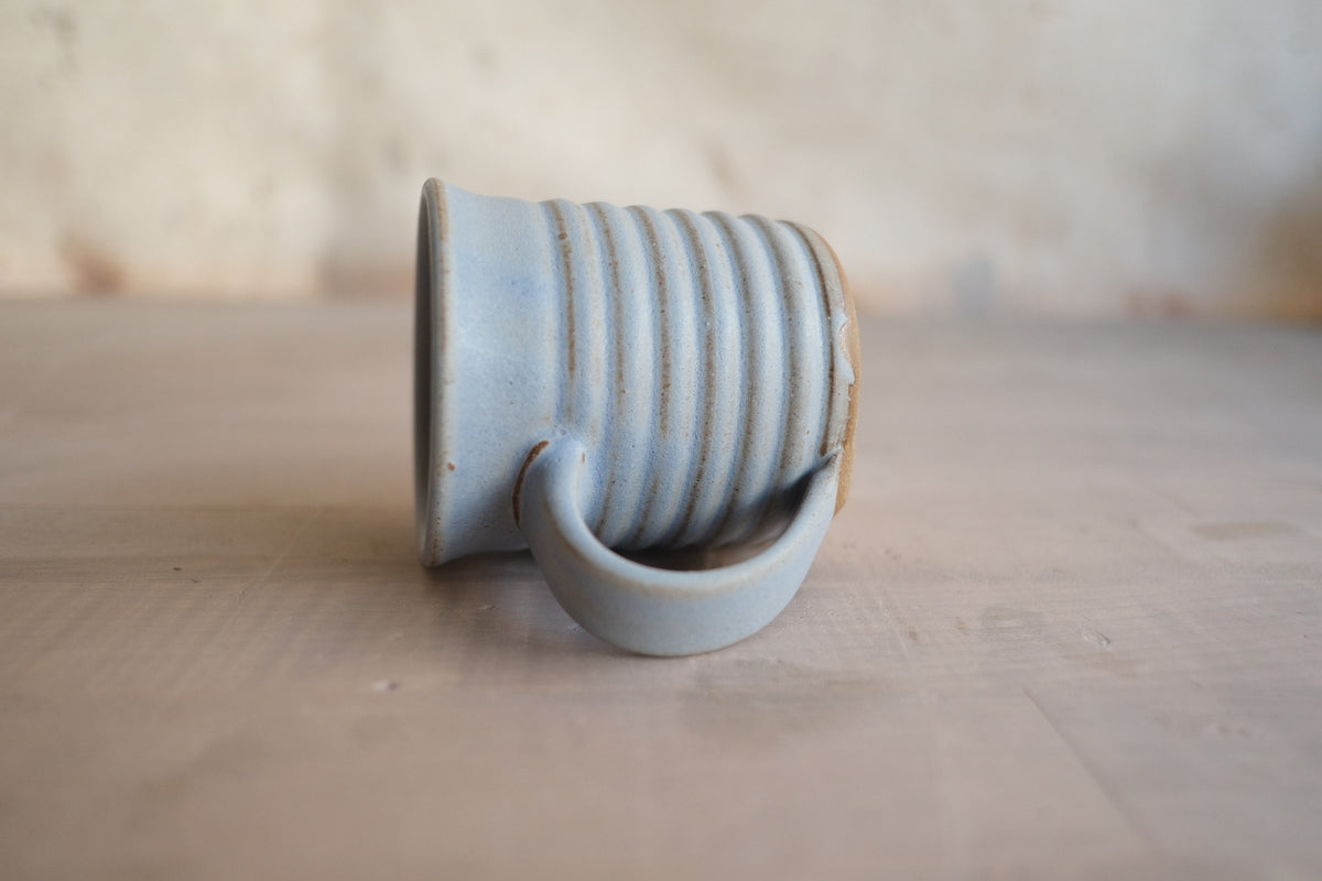 The Little Mug: eye-level view of a ribbed ceramic cup lying horizontally on its side, showing base and handle.