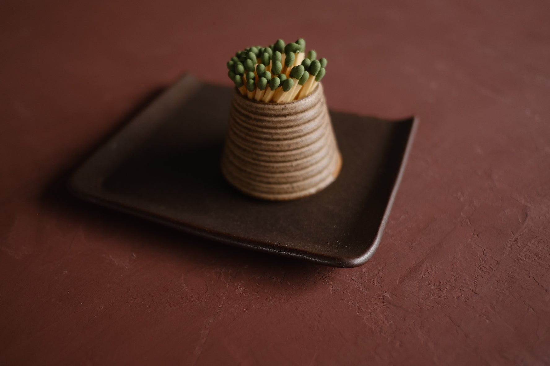 Textured Striker with ribbed exterior holding green matches, resting on a dark square ceramic tray.