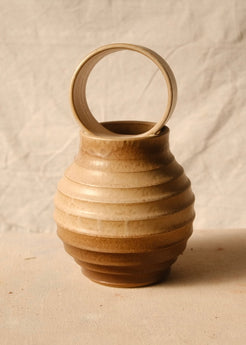 O Orbe Vase, a rounded ceramic vase with ribbed tiers and a large loop handle atop its opening, seen straight-on.