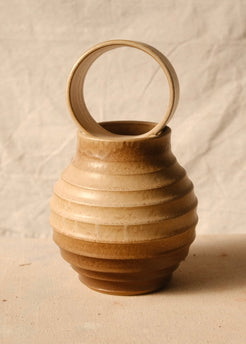 O Orbe Vase lit from the side on textured canvas, showing the raised ribs along the bulbous body and open ring handle.