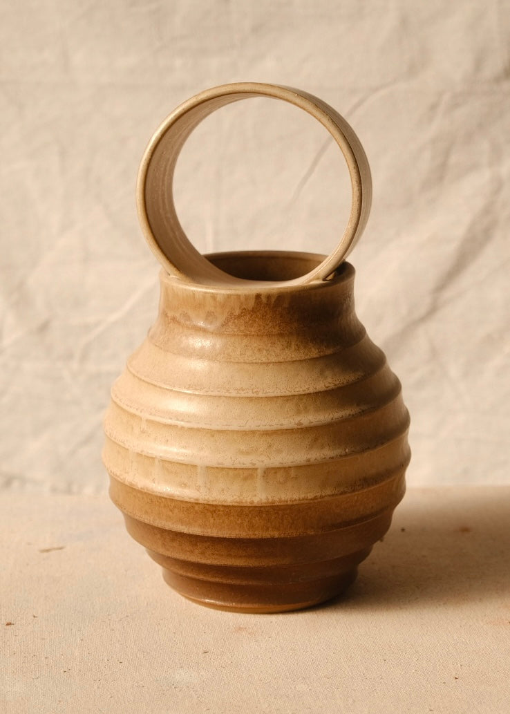 O Orbe Vase lit from the side on textured canvas, showing the raised ribs along the bulbous body and open ring handle.