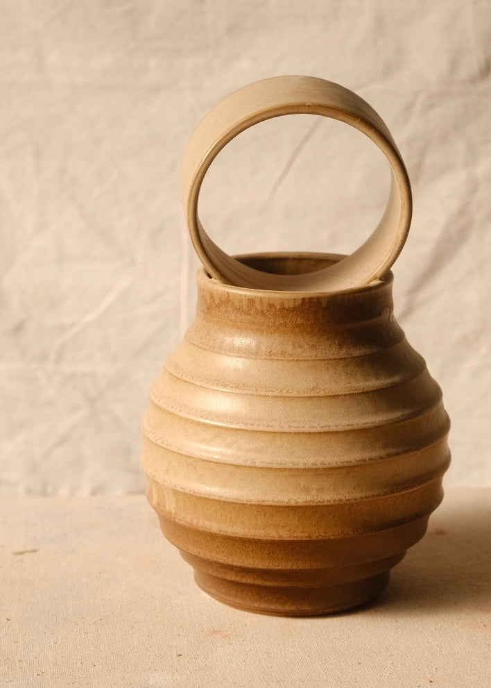 O Orbe Vase centered in warm studio lighting, accentuating the banded horizontal ridges and circular loop handle above.