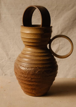 Encircled Vase with a ceramic ring resting in the rim and a round loop handle on the right, set on neutral cloth.