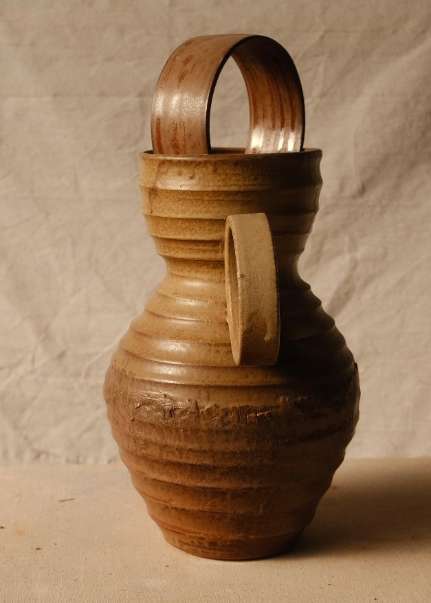 Encircled Vase angled with its circular handle facing front, showing horizontal ridges and a ceramic arch in the rim.