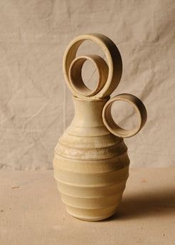 Within Vase with concentric ring stopper, horizontal ridges, and round side handle pointing right on pale fabric.