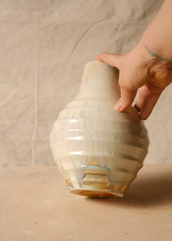 Woodfire Ripple Vase, held by a hand at the rim to show scale, tilted slightly to reveal the lower glazed ridges and foot.
