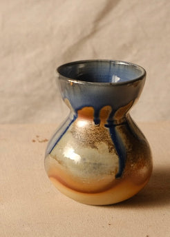 Woodfire Sake Carafe #1 on canvas fabric, showing its flared rim and glazed bulbous body with dark drips.