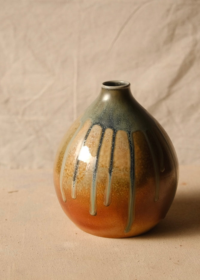 Woodfire Orbe Vase shown from the front, glaze drips streaming down its round orange-toned body against draped linen.