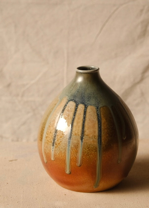 Woodfire Orbe Vase viewed in full against a draped textile backdrop, resting flat on a light cloth surface.