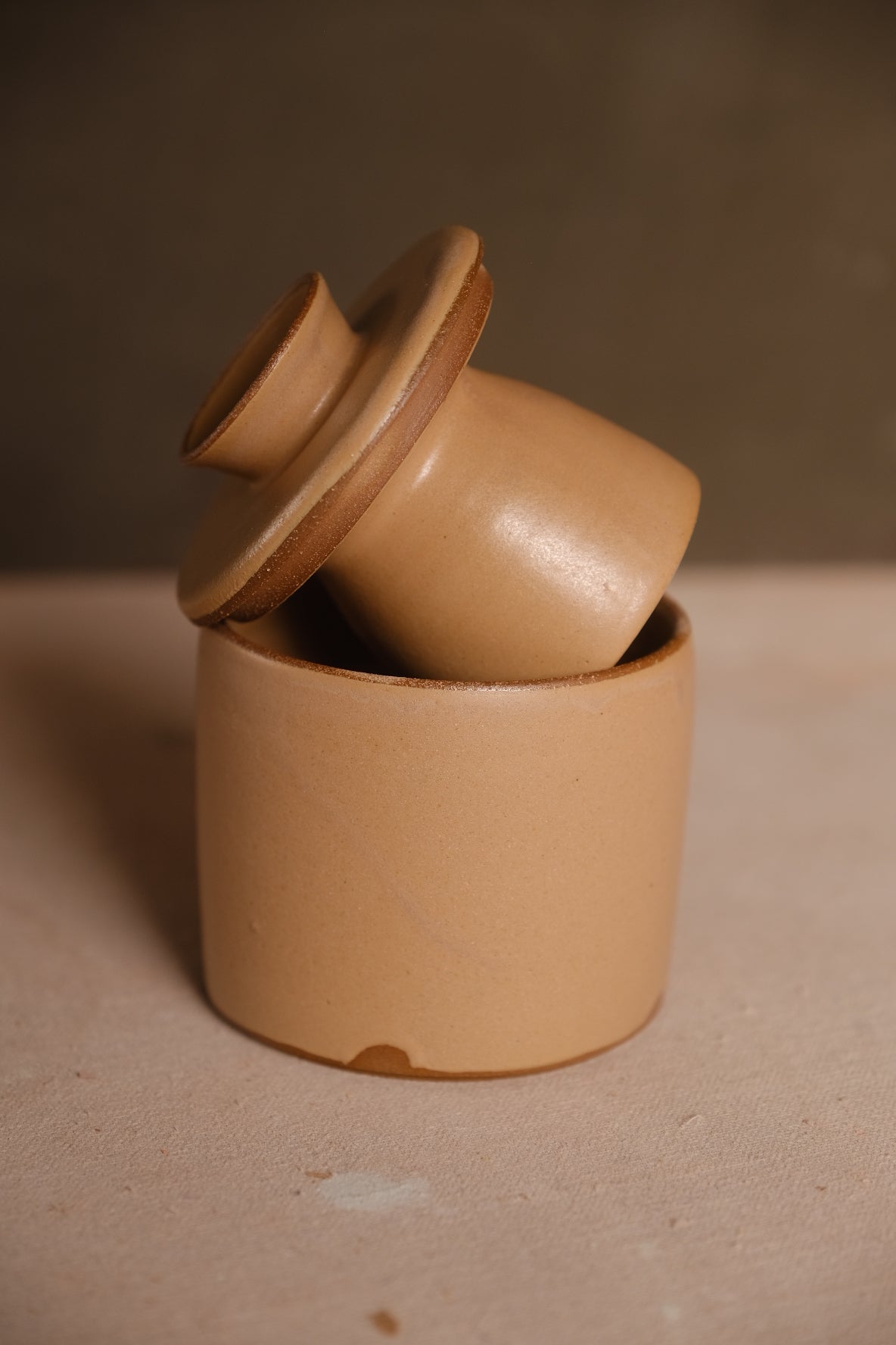 Butterbell crock with smooth tan glaze, bell lid tipped upside down inside the base, showing unglazed clay margins.