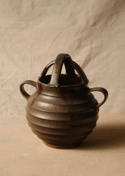 Regal ribbed stoneware vase angled forward to show the open rim beneath intersecting arch handles and side loops.