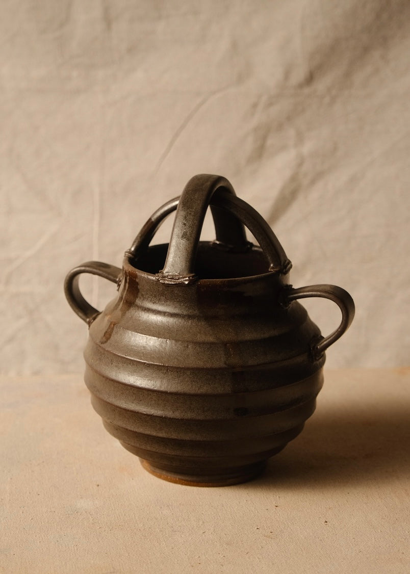 Regal ribbed stoneware vase angled forward to show the open rim beneath intersecting arch handles and side loops.