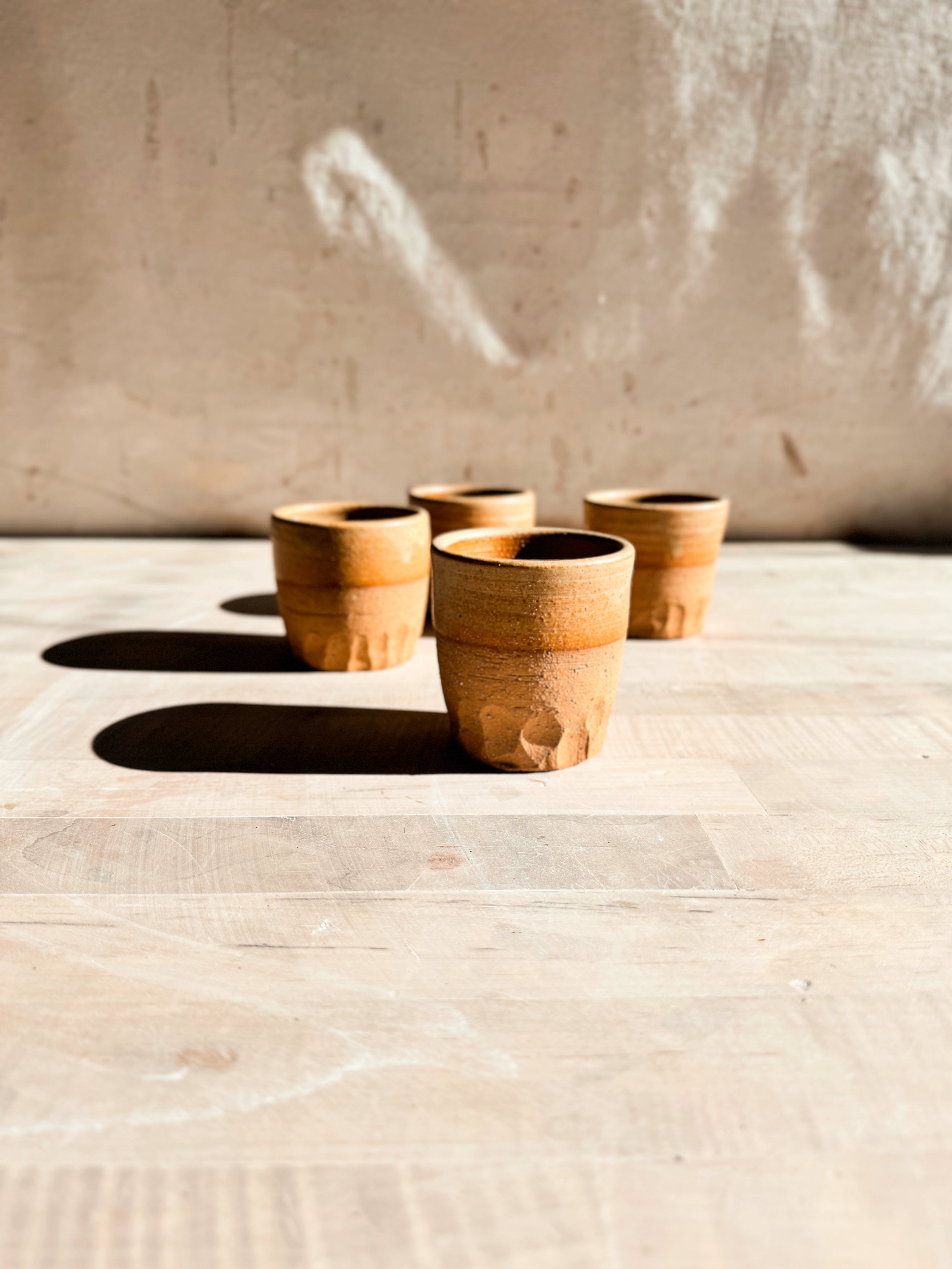 Aura Sipper cup stands centered in the foreground, with three matching ceramic cups arranged in a row behind on wood.