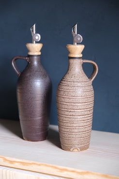 Tejas Oil Bottle set of two on a wooden shelf, dark brown and light speckled stoneware, metal spouts with wood collars.