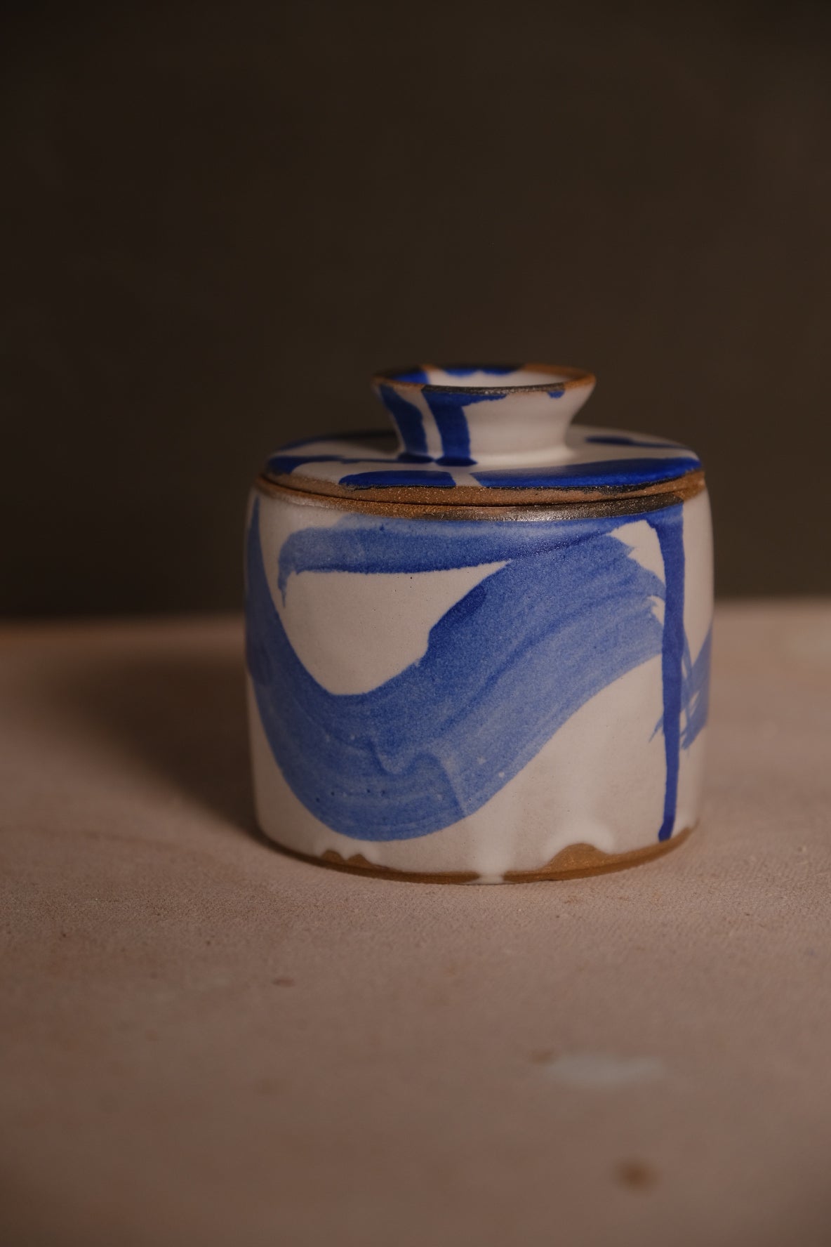 Butterbell closed with lid in place, featuring wide blue brushstroke glaze over white ceramic and an exposed clay foot.