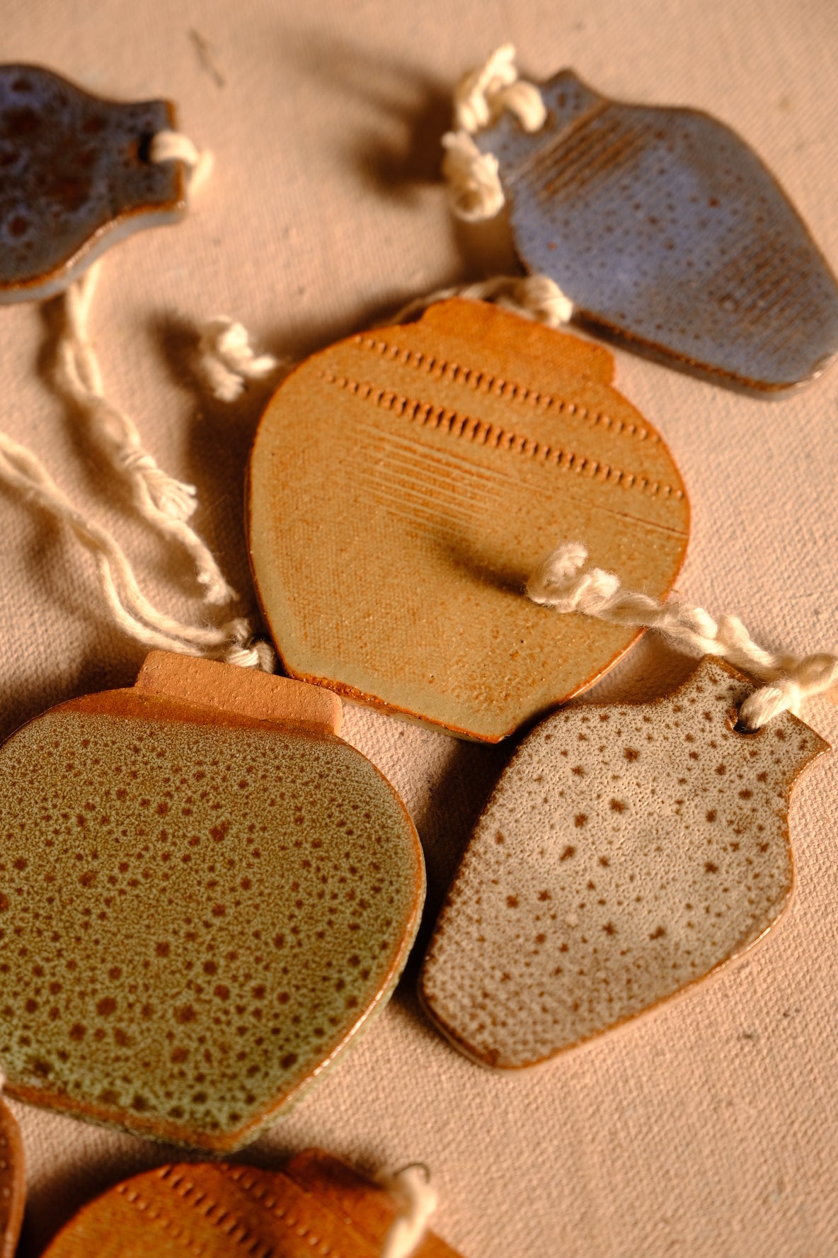 Ceramic ornaments in round jar and vase shapes displaying speckled green, cream, and carved clay finishes on fabric.