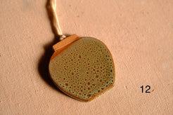 Ceramic ornament wide rounded jar silhouette with speckled olive green glaze and unglazed rim, numbered twelve.