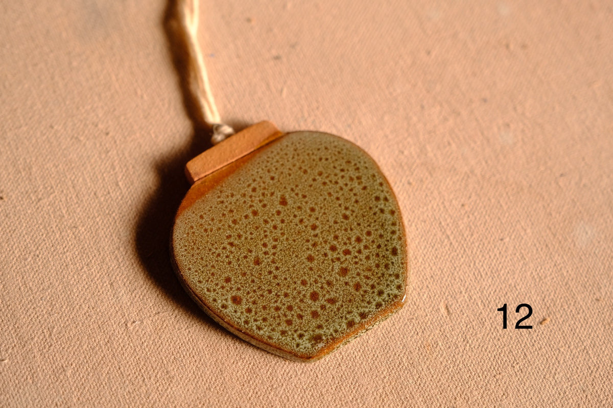 Ceramic ornament wide rounded jar silhouette with speckled olive green glaze and unglazed rim, numbered twelve.
