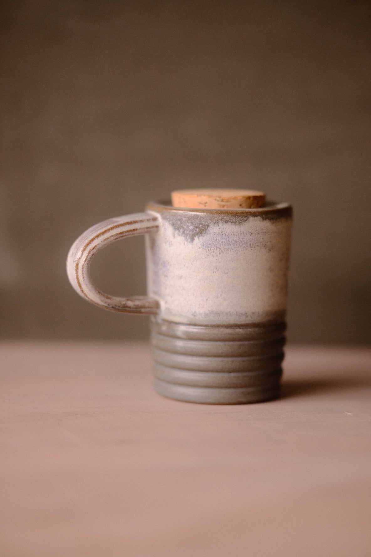 Stormy Sky Traveller travel mug with cork lid, handle on left. Pale grey top half, ridged grey bottom on a pale surface.