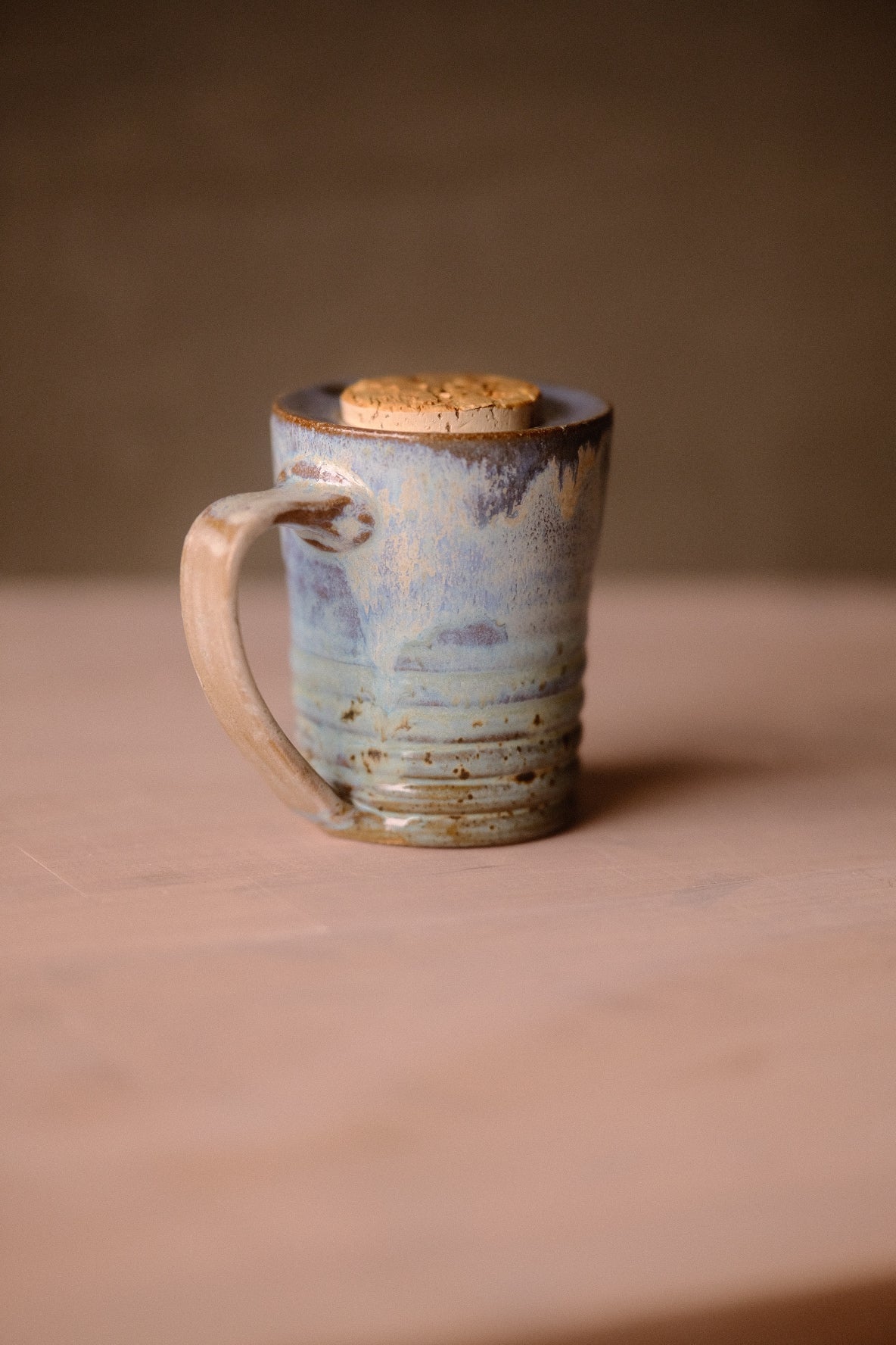 Secret Cenote Traveller Mug standing on a wooden surface, showing its left-facing looped handle, ribbed base, and flush cork.