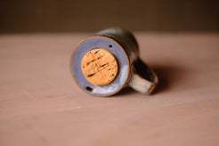 Secret Cenote Traveller Mug tilted forward to reveal the recessed ceramic top, central cork stopper, and dual sip holes.