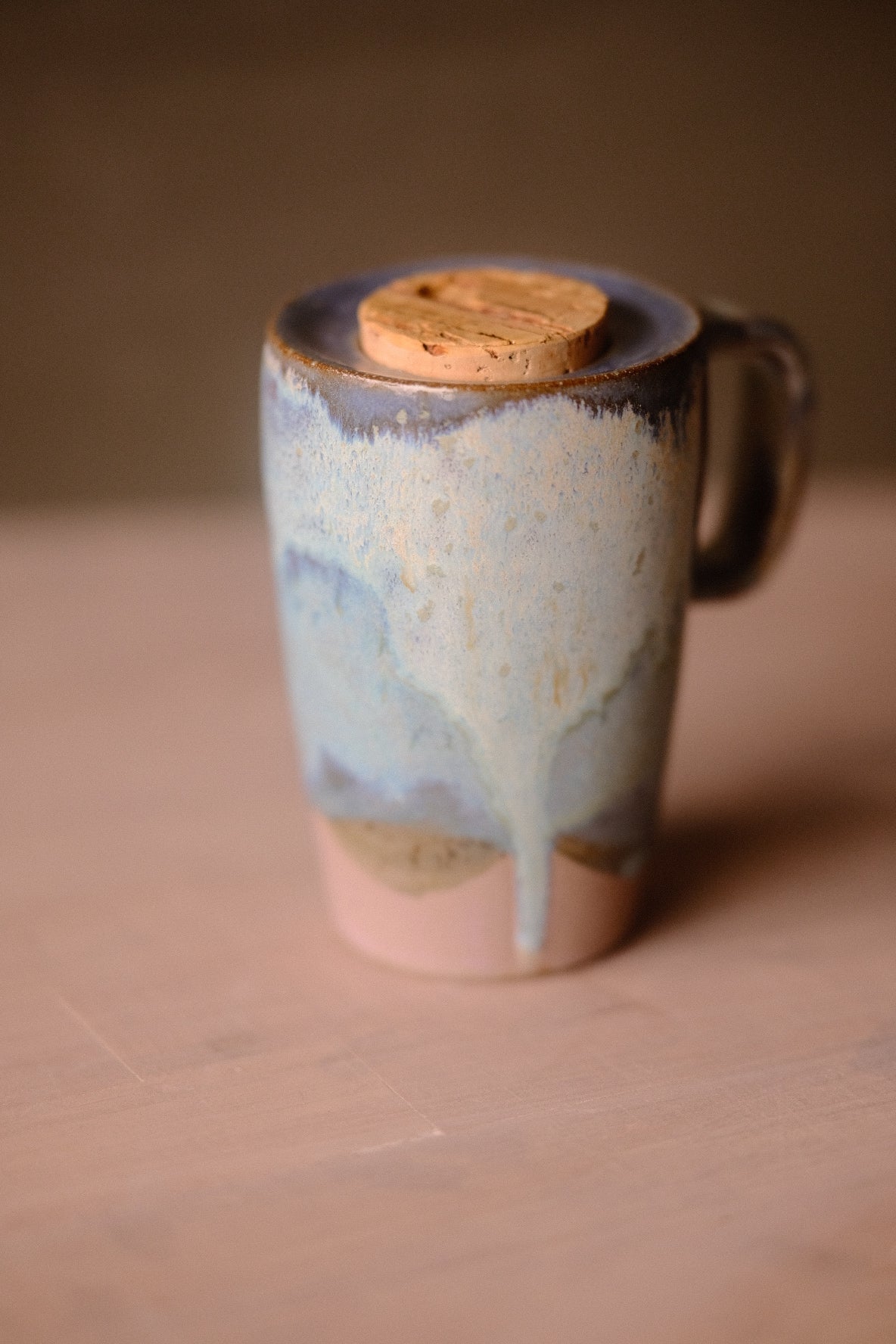 Secret Cenote Tall Traveller ceramic travel mug standing on a table, handle on right, showing glazed drips and cork stopper.